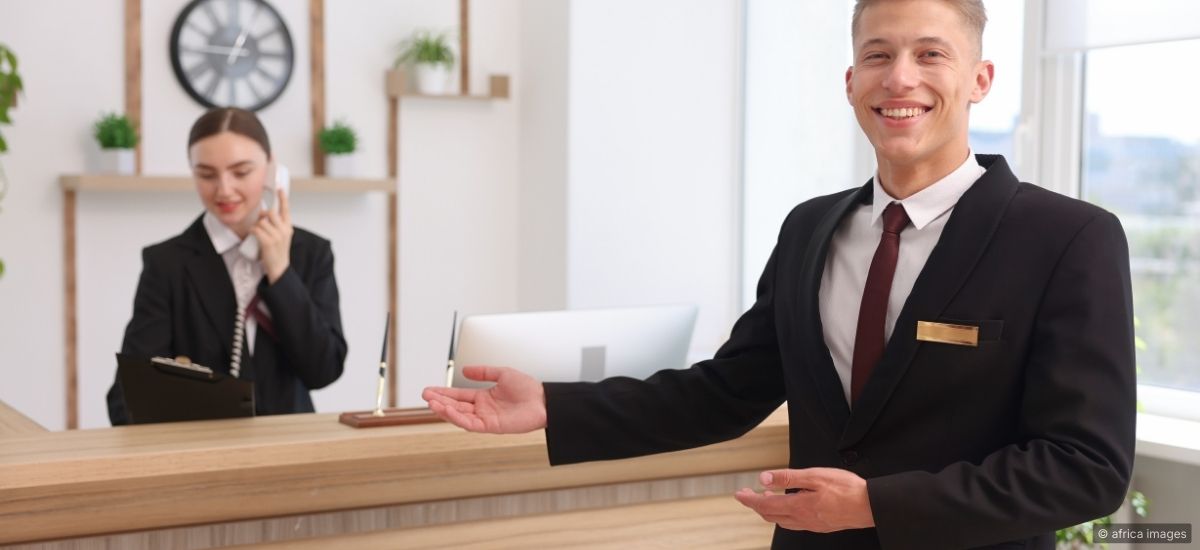 A concierge standing at attention near a hotel entrance with open body language and a composed expression
