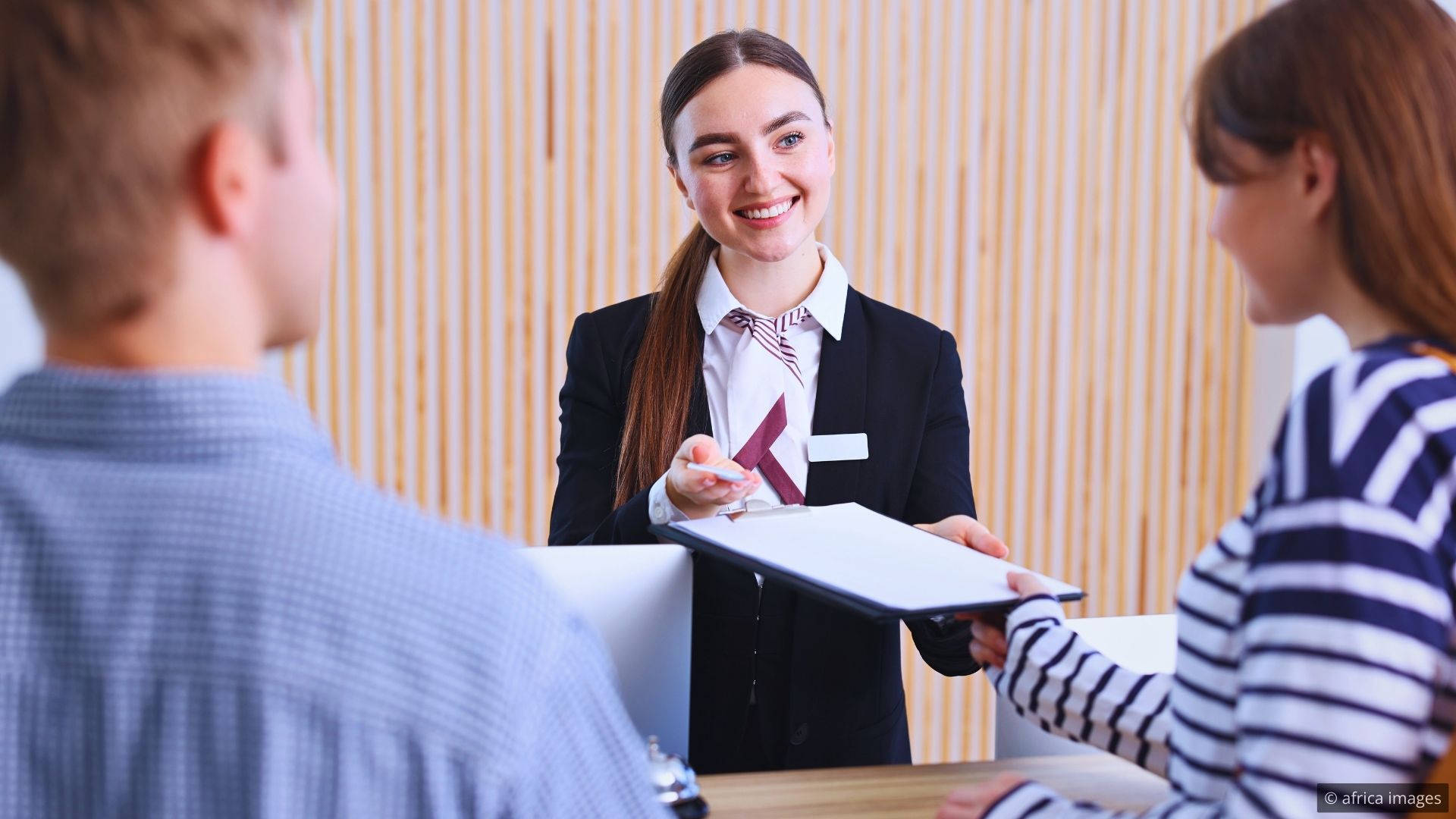Hotel lobby with a front desk agent greeting a guest with direct eye contact and confident posture