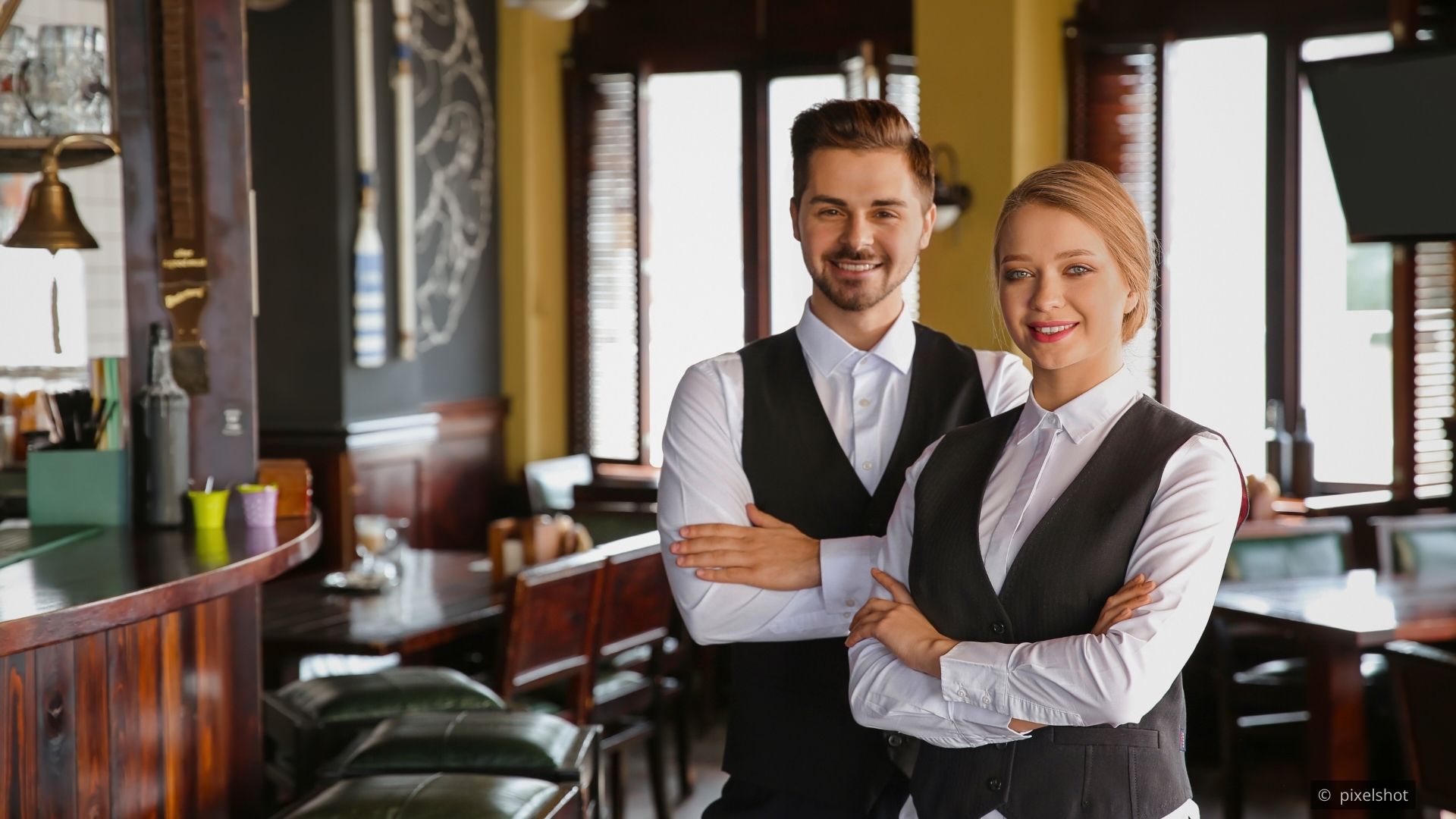 A restaurant server speaking with guests at a table with composed posture and a warm but professional expression