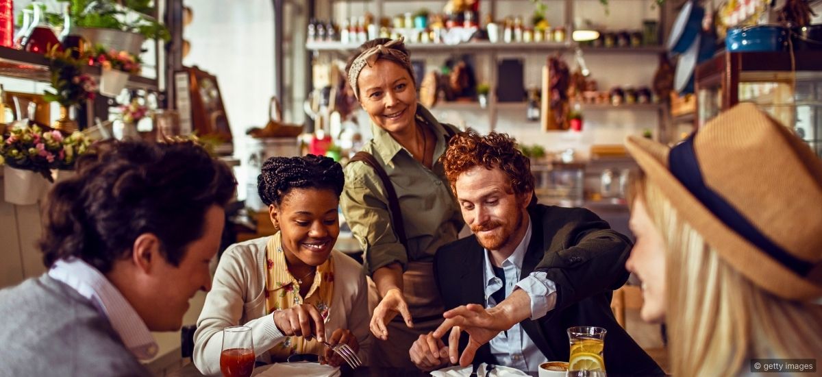 A fine dining server standing at the periphery of a dining room, observing table dynamics before approaching
